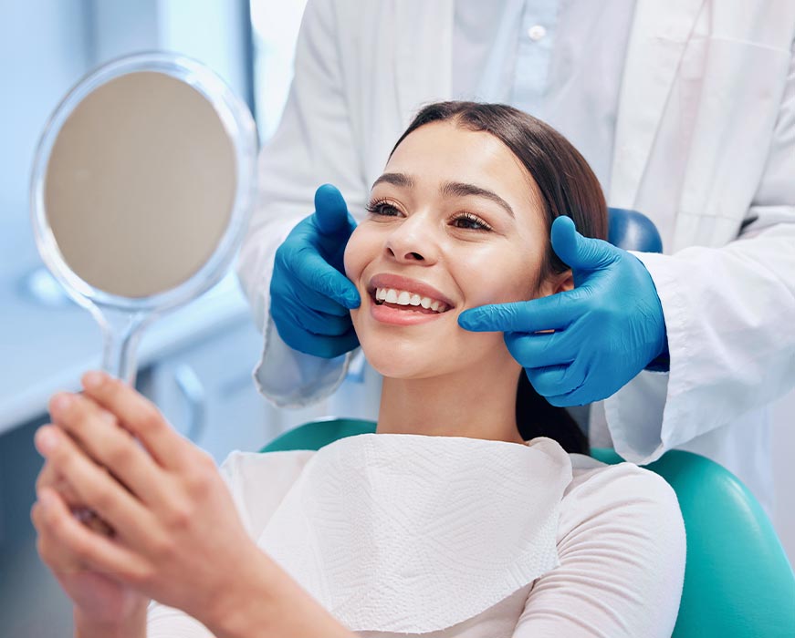 The image depicts a woman sitting in a dental chair with her eyes closed, receiving dental care from a professional who is adjusting her mouthpiece.