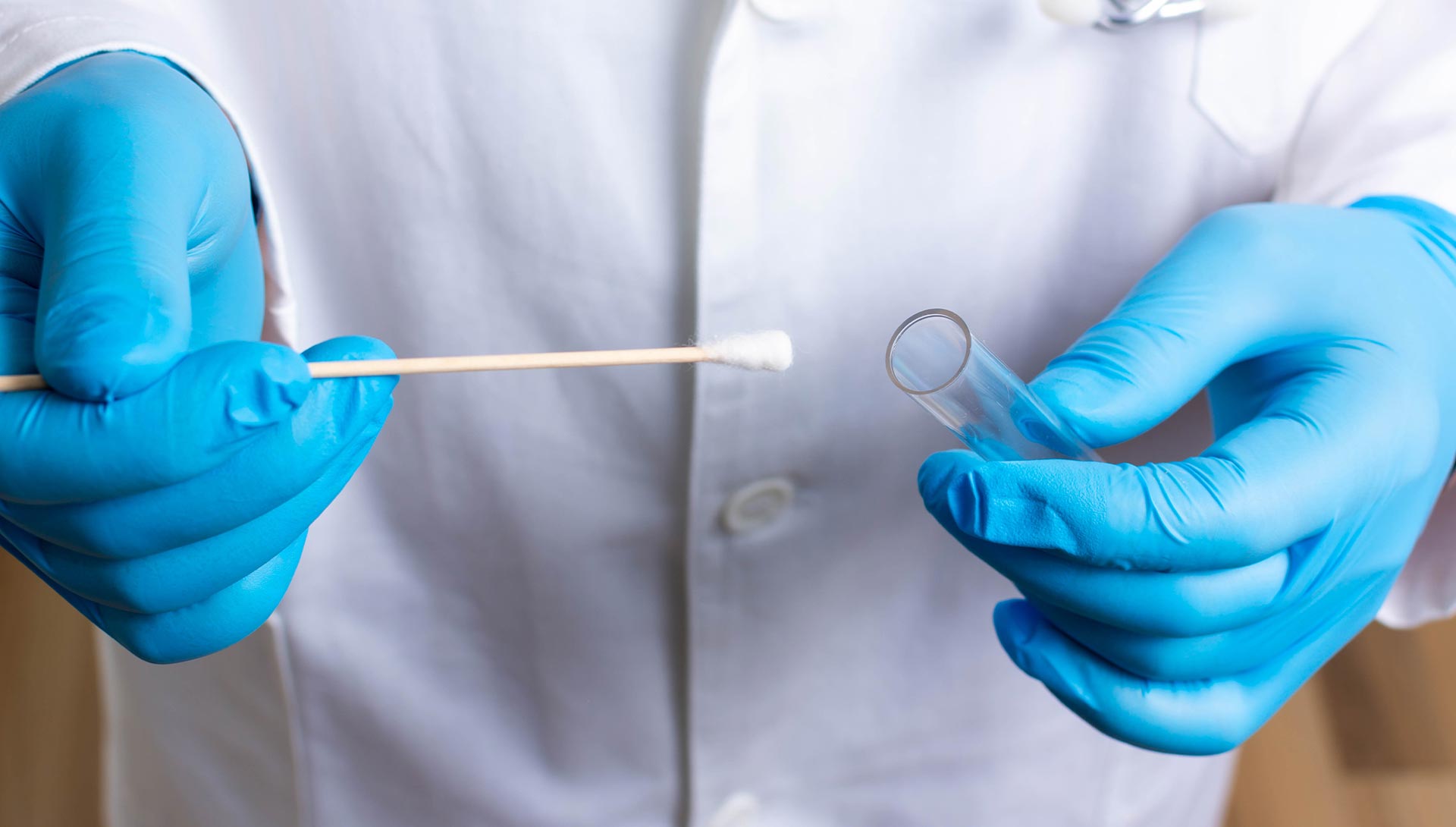 A scientist in blue gloves holding a test tube with a clear substance next to a beaker with a blue substance.