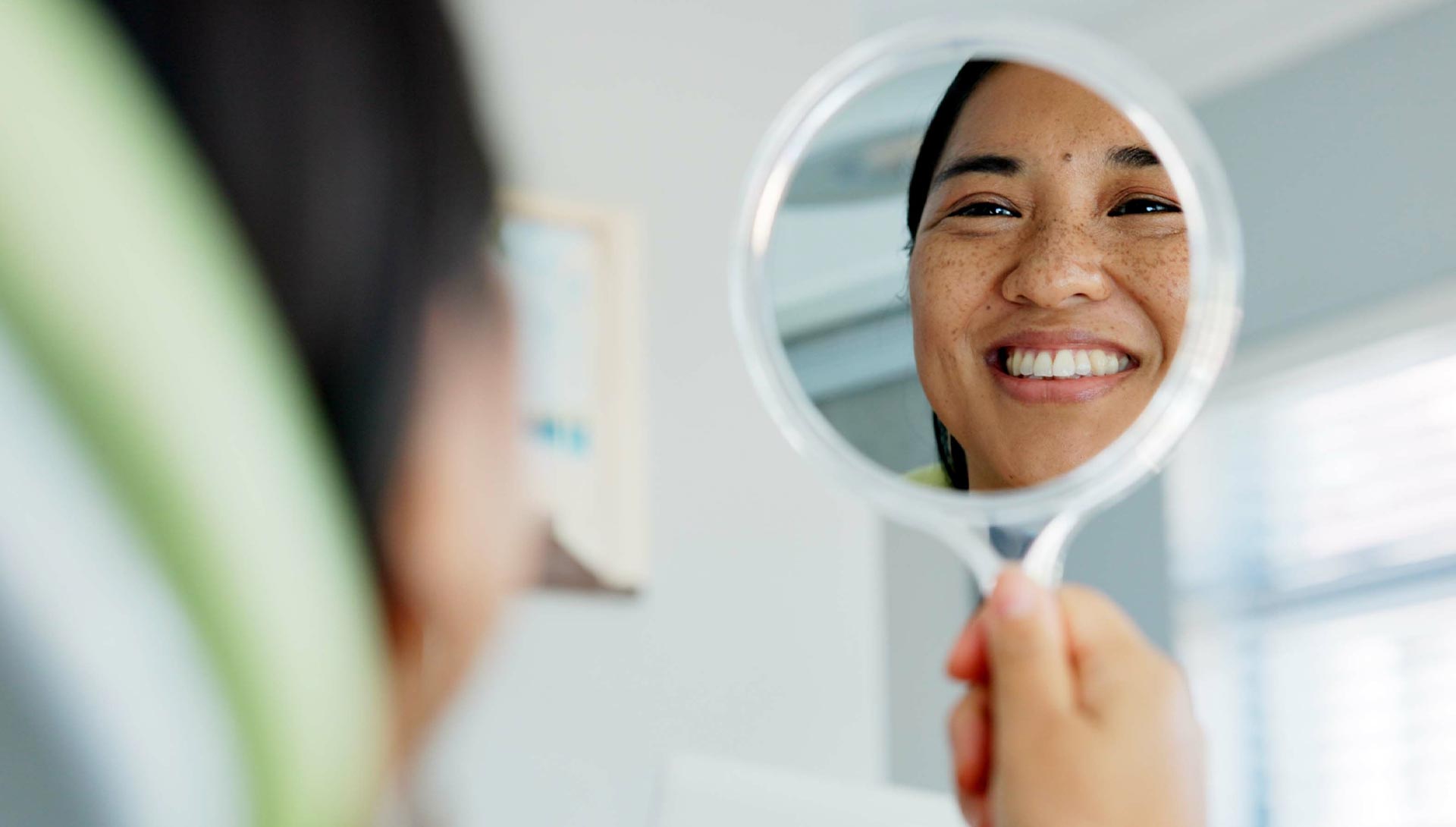 Woman looking at her reflection in a round mirror with a smile on her face.