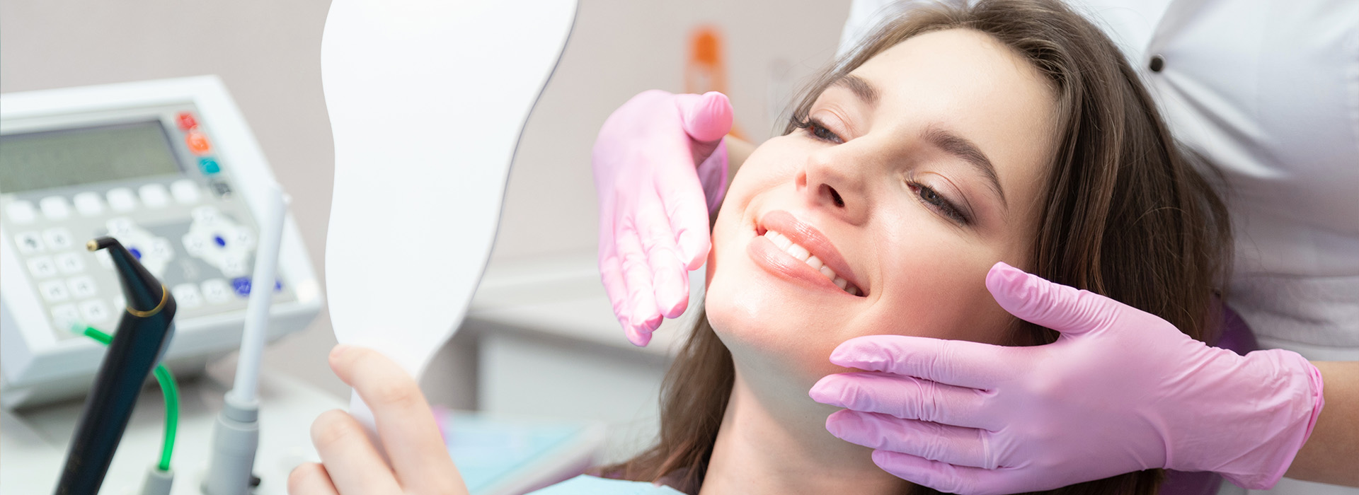A woman seated in a dental chair receiving dental care with a smiling hygienist attending to her.