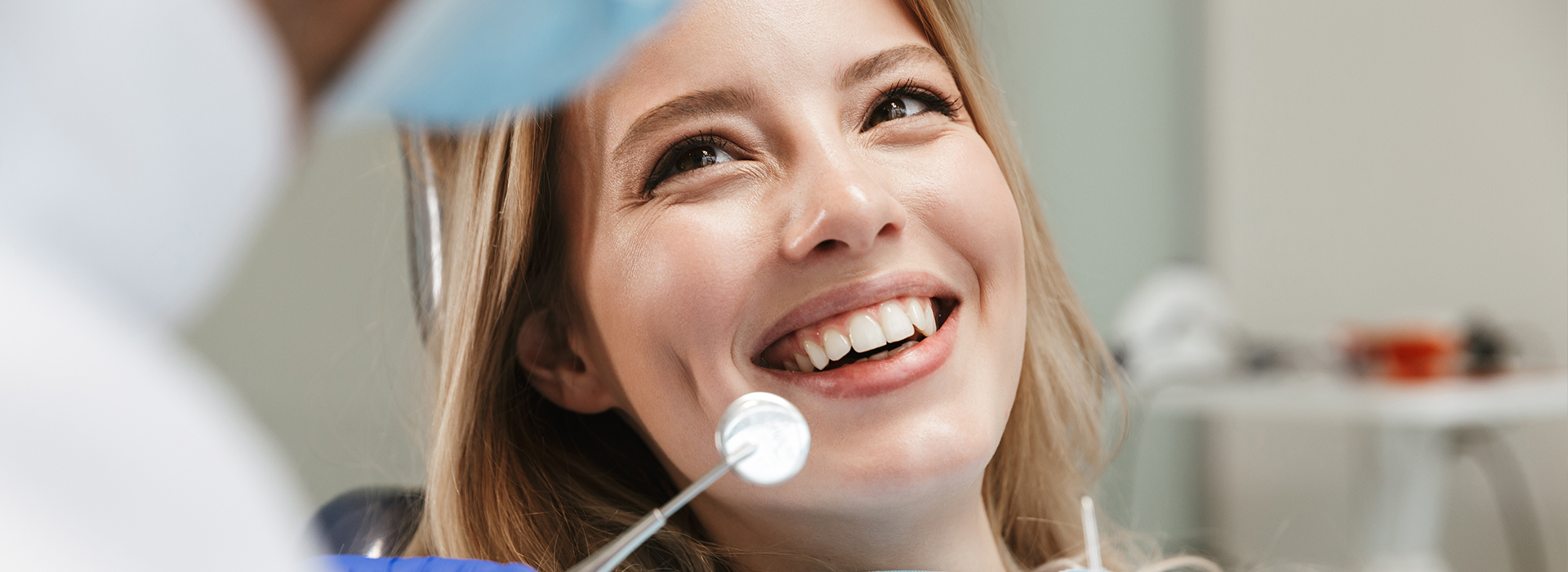 A woman with a big smile sitting in a dental chair while getting her teeth cleaned by a dentist.