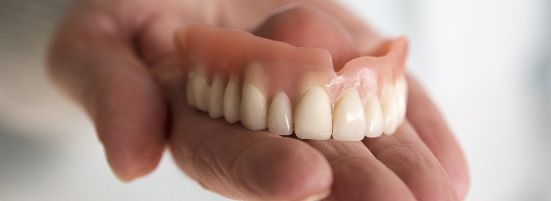 The image shows a person s hand holding up a set of dentures with visible teeth, likely for dental examination or display purposes.