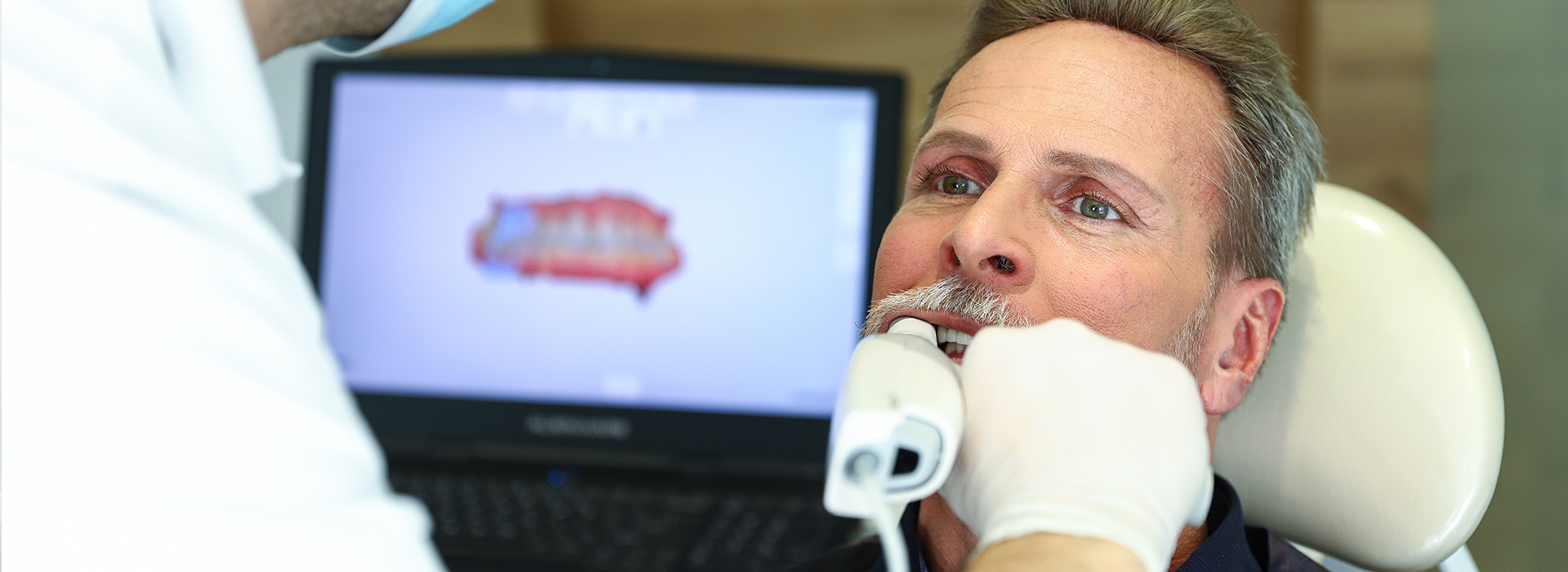 The image shows a man receiving dental care, with a dentist performing a procedure on him while he sits in a chair.