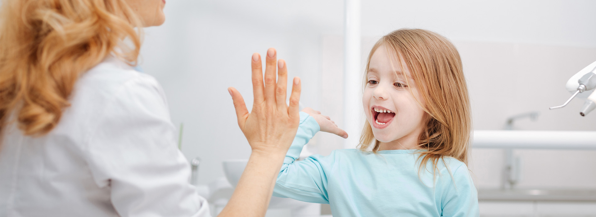 A young girl clapping her hands while an adult watches with a smile.