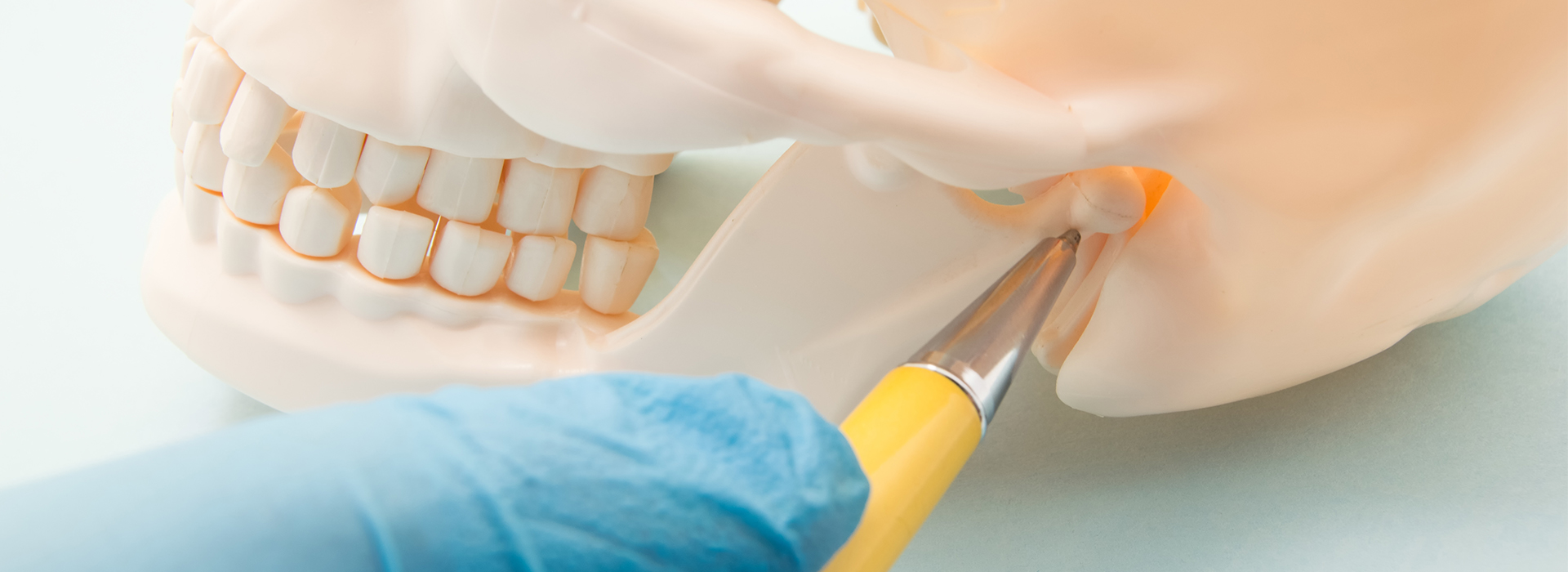 The image shows a close-up of a dental implant procedure with a focus on the implant being placed into a model mouth, while a person s hand holds the implant in place using a dental tool.