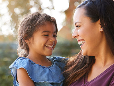 Woman and child smiling at camera, outdoor setting, daytime.