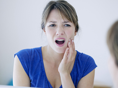 A woman with her mouth open, expressing discomfort, while looking at her reflection in a mirror.