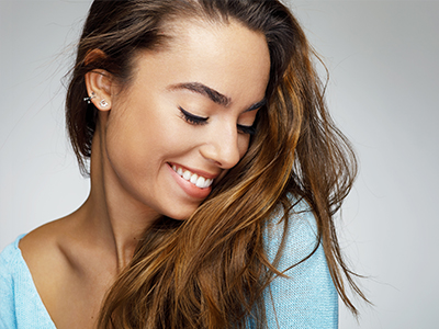 The image features a woman with long hair smiling at the camera, wearing a blue top, against a white background.