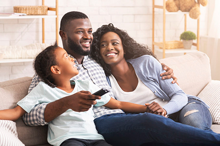 A family of four on a couch with a warm smile, watching television together.