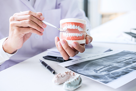 The image shows two separate photographs placed side by side  on the left, a dental professional wearing medical attire is holding a model mouth with teeth  on the right, a hand is holding a small cup filled with dental implants in front of an array of dental models and tools.