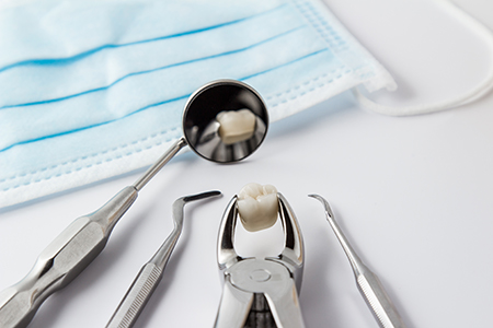 The image shows a collection of dental instruments including a toothbrush, tweezers, and a small drill, all placed on a surface with a blue cloth underneath, suggesting a dental care context.