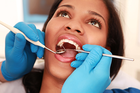 A woman receiving dental treatment with a dental hygienist performing the procedure, wearing blue gloves and using dental instruments.