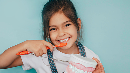 A young girl brushing her teeth with an oversized toothbrush.