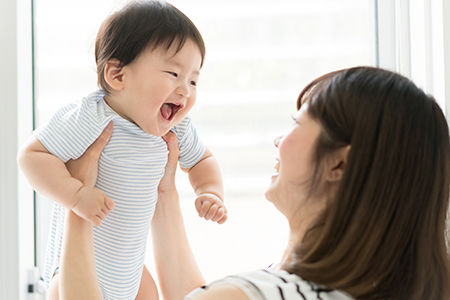 The image shows a woman holding a baby while smiling, with both looking at the camera.