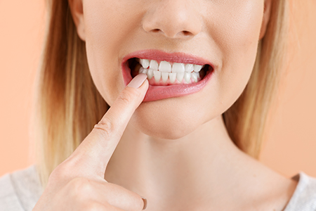 A woman with her finger on her teeth, possibly brushing them, against a white background.