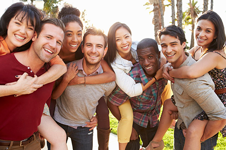 This is a color photograph showing a group of people posing together outdoors during daylight. They appear to be friends or family members, with some standing and others hugging. The setting suggests a casual gathering, possibly for an event or celebration.