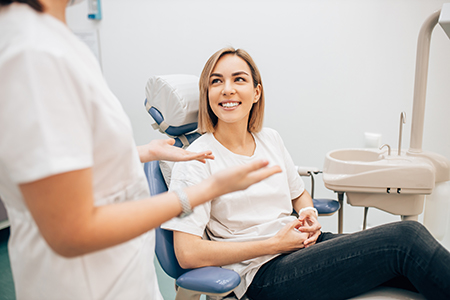 A woman sitting on a dental chair with a smile, receiving dental care from a dentist in a professional setting.
