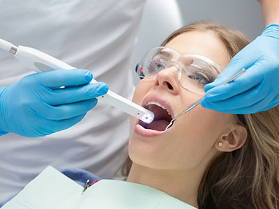 A woman receiving dental treatment with a machine attached to her mouth while a professional attends to her.