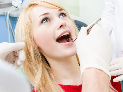 A woman receiving dental care with a dentist using a drill on her teeth.