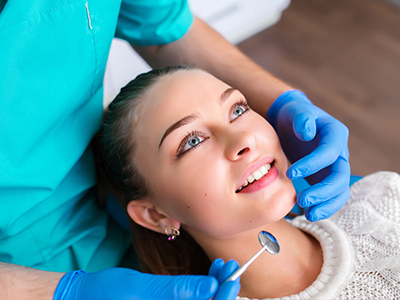 A smiling woman with blue eyes receiving dental care from a dental professional wearing a medical mask and stethoscope.