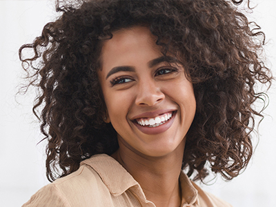 A smiling woman with curly hair and a joyful expression against a white background.